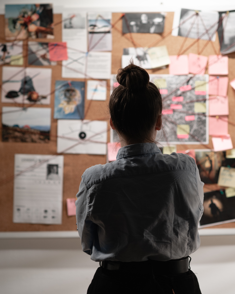 Person analyzing a corkboard with notes.