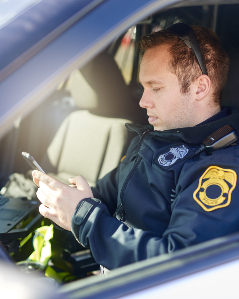 Police officer using phone in patrol car.